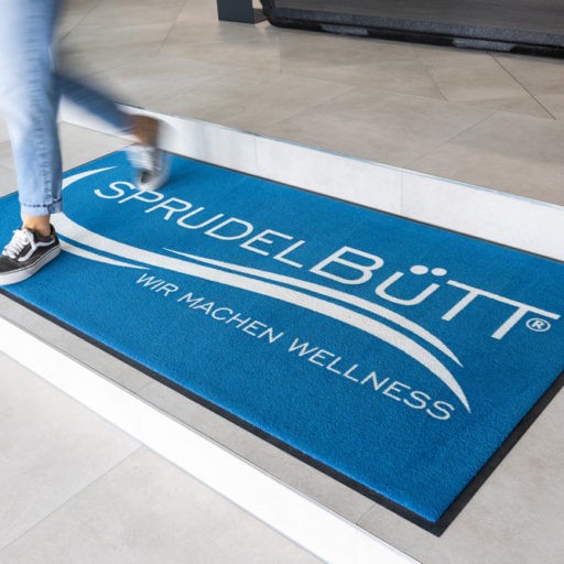 Blaue Fußmatte mit Wellness-Logo.